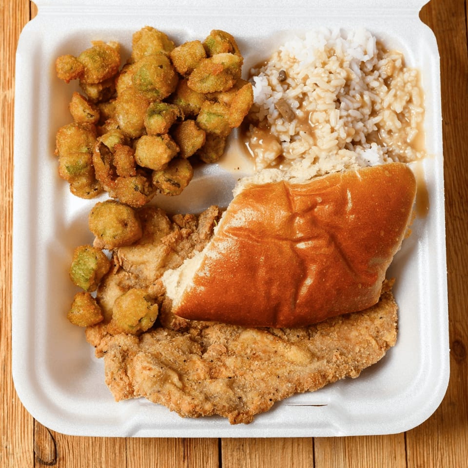 Fried chicken, fried okra, rice with gravy, and a bun in a white takeout container.